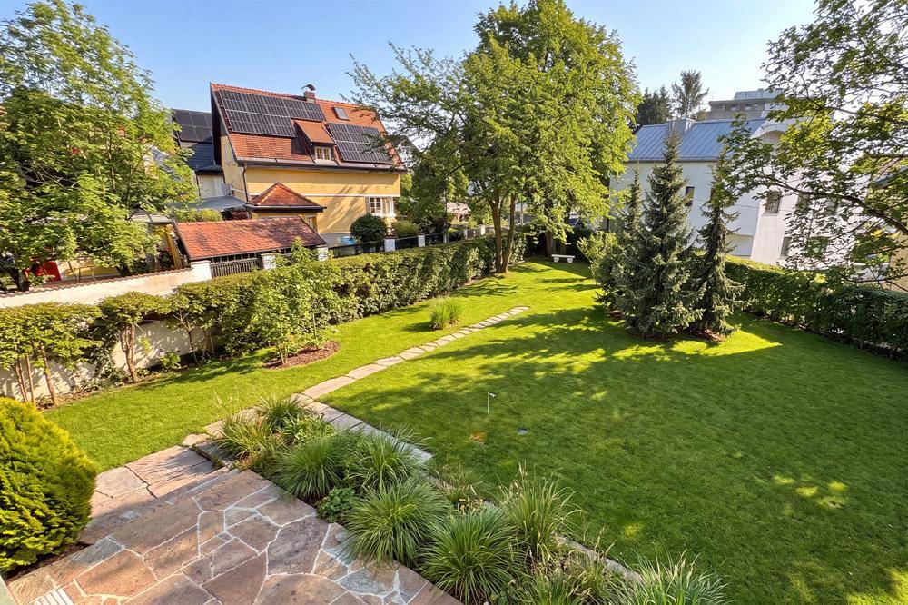 Weitläufiger, gepflegter Garten mit Rasenflächen, Bäumen und Steinpfaden.