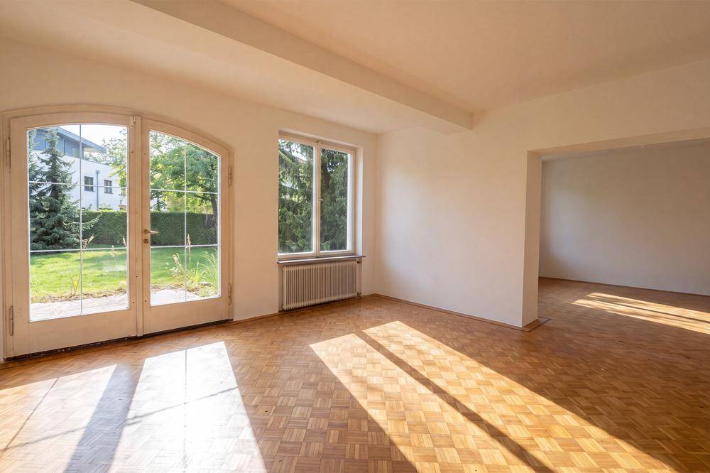 Geräumiges, leeres Wohnzimmer mit Fischgrätparkett und Zugang zum Garten.