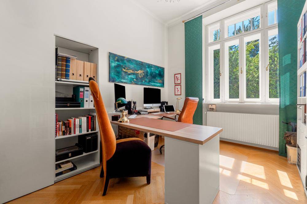 Helles Arbeitszimmer mit großem Fenster, Holzparkett und modernen Büromöbeln.