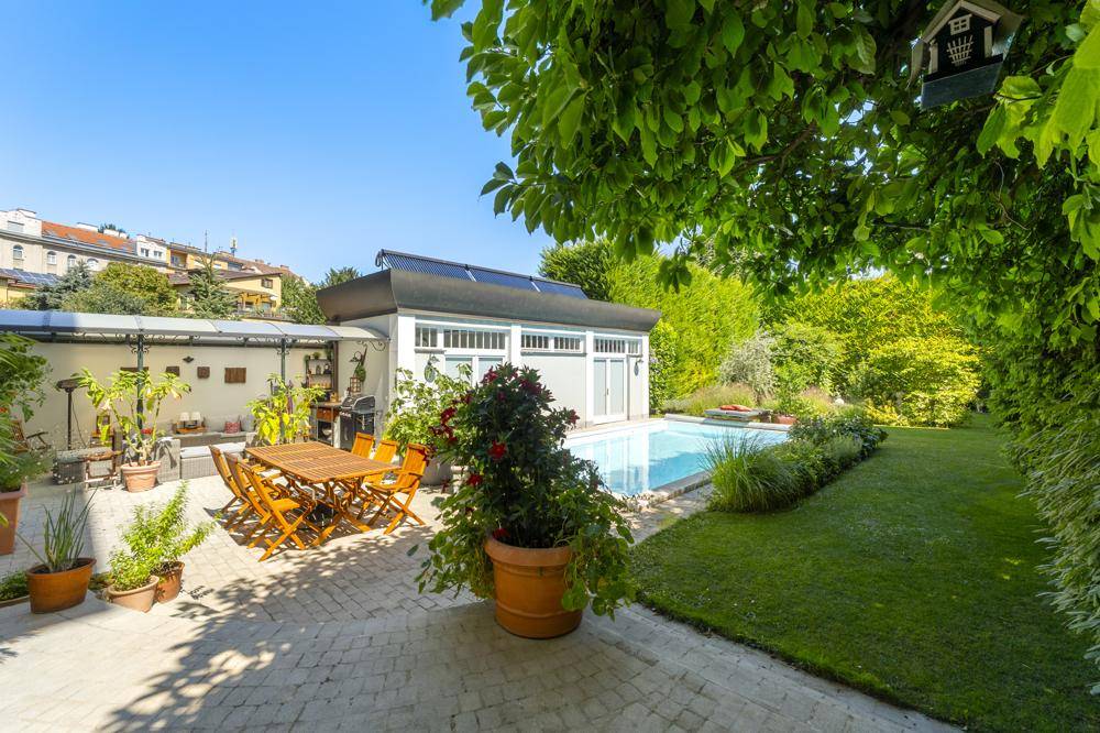 Sonnige Terrasse mit Esstisch im Freien, Grillbereich und Blick auf den Pool.