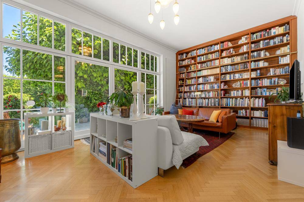 Helles Wohnzimmer mit raumhohen Fenstern, großem Bücherregal und gemütlicher Sitzecke.