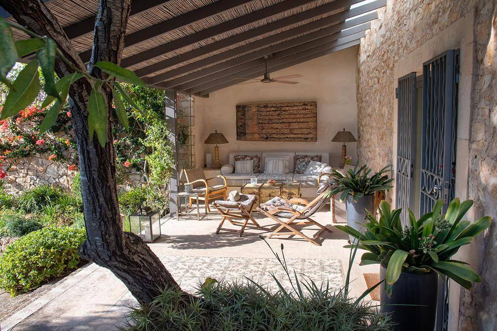 Überdachte Terrasse mit bequemen Sitzgelegenheiten, Deckenventilator und mediterraner Bepflanzung.