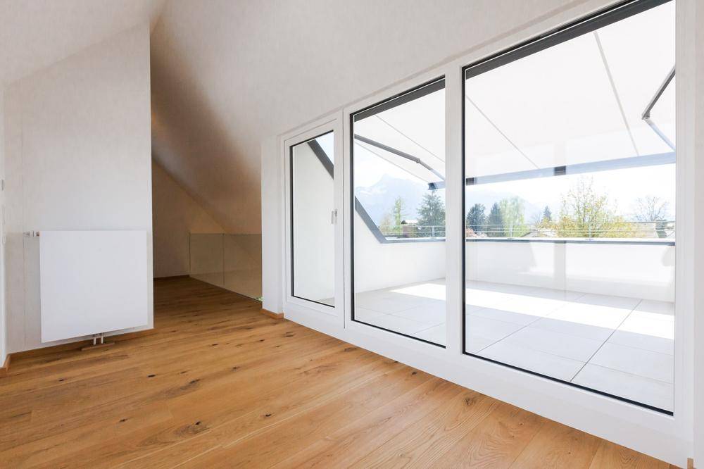Heller Raum mit großen Fenstern, Holzboden und Zugang zu einer Terrasse mit Bergblick.