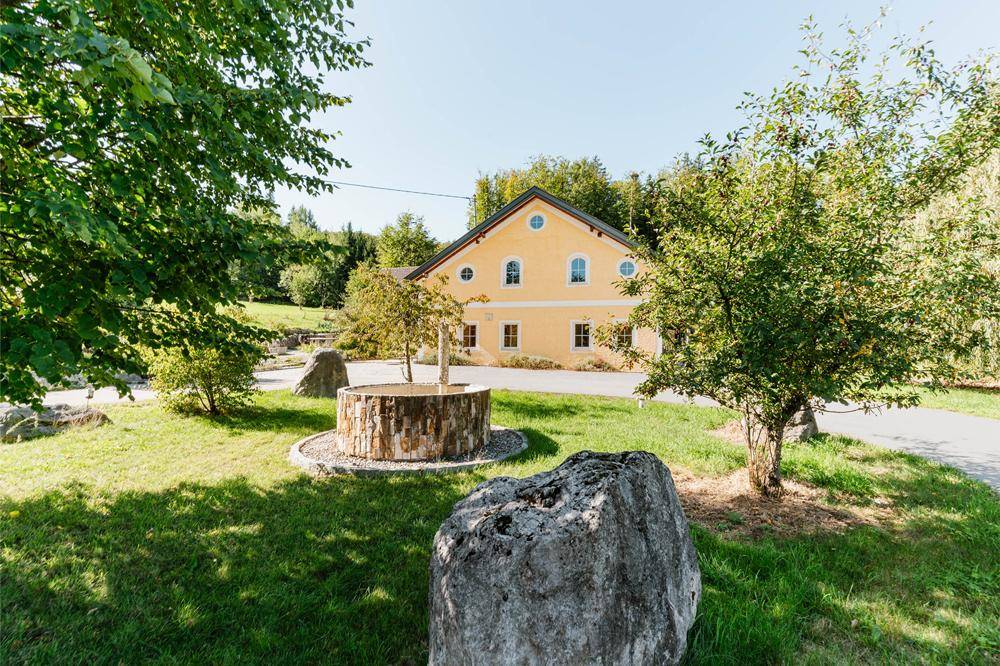 Gelbes Landhaus mit traditioneller Architektur, umgeben von gepflegtem Garten und Bäumen.