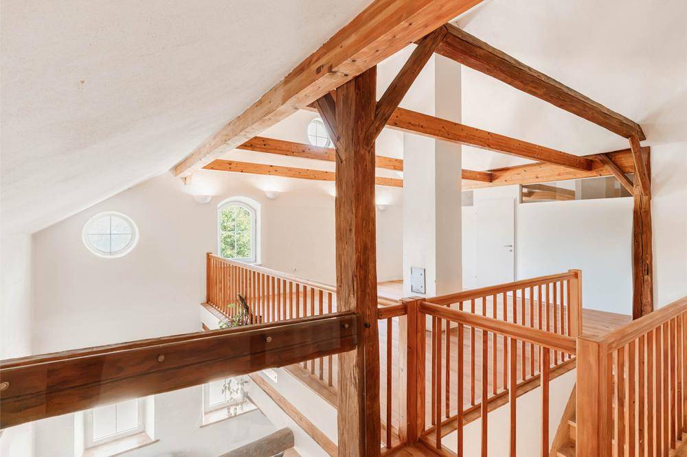 Helle Galerie mit Holzbalken und Geländer, die den Blick in den unteren Bereich freigibt.