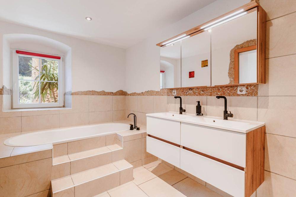 Modernes Badezimmer mit Doppelwaschbecken, Badewanne und Fenster, in hellen Farbtönen.