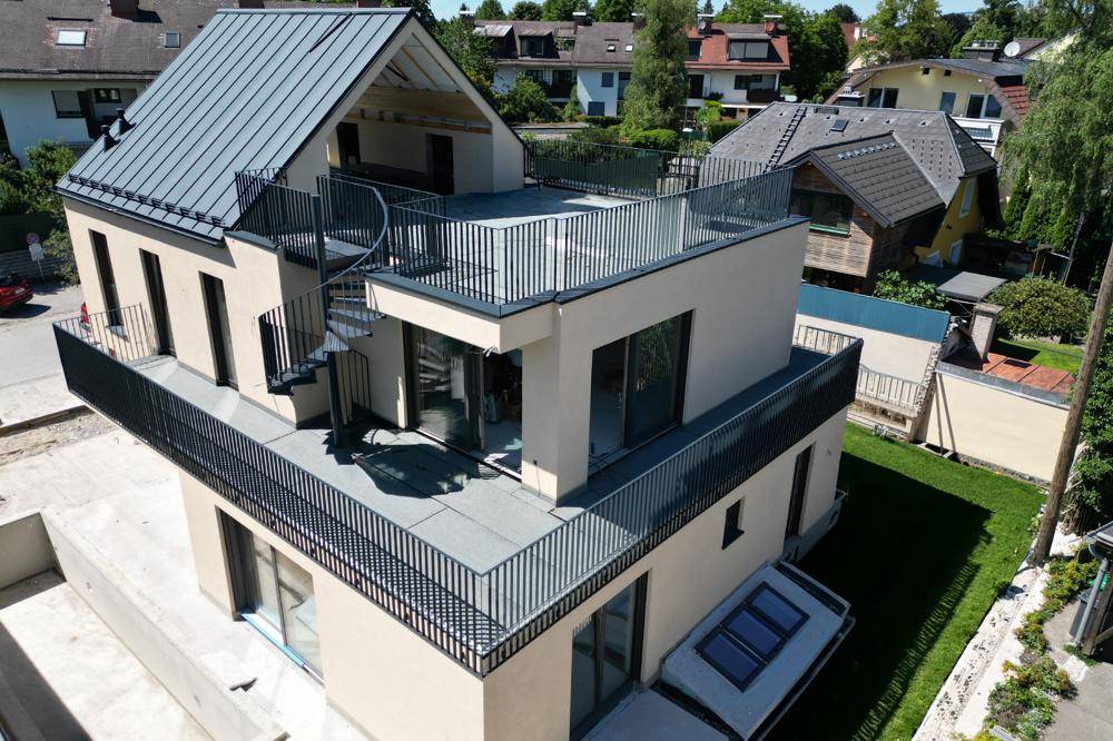 Luftaufnahme eines modernen Wohnhauses mit mehreren Terrassen, Wendeltreppe und Gartenbereich.