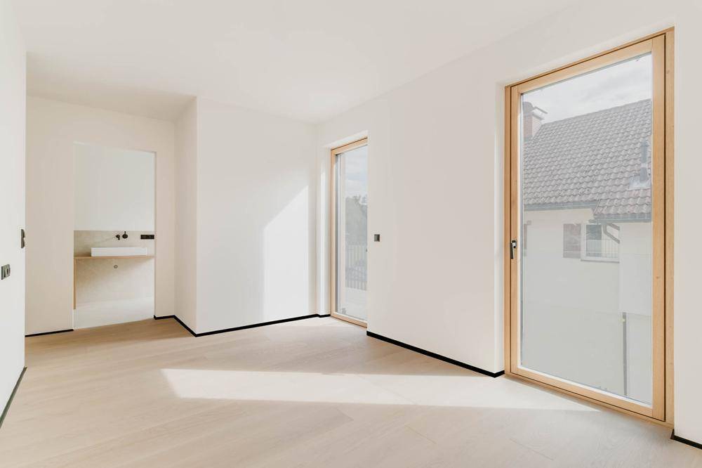 Heller Raum mit Holzboden und hohen Fenstern, angrenzend an ein modernes Badezimmer.