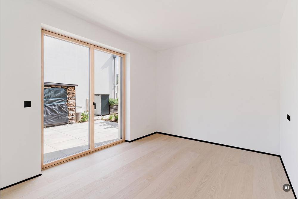 Geräumiger, heller Raum mit Holzboden und Schiebetüren zu einem gepflasterten Außenbereich.