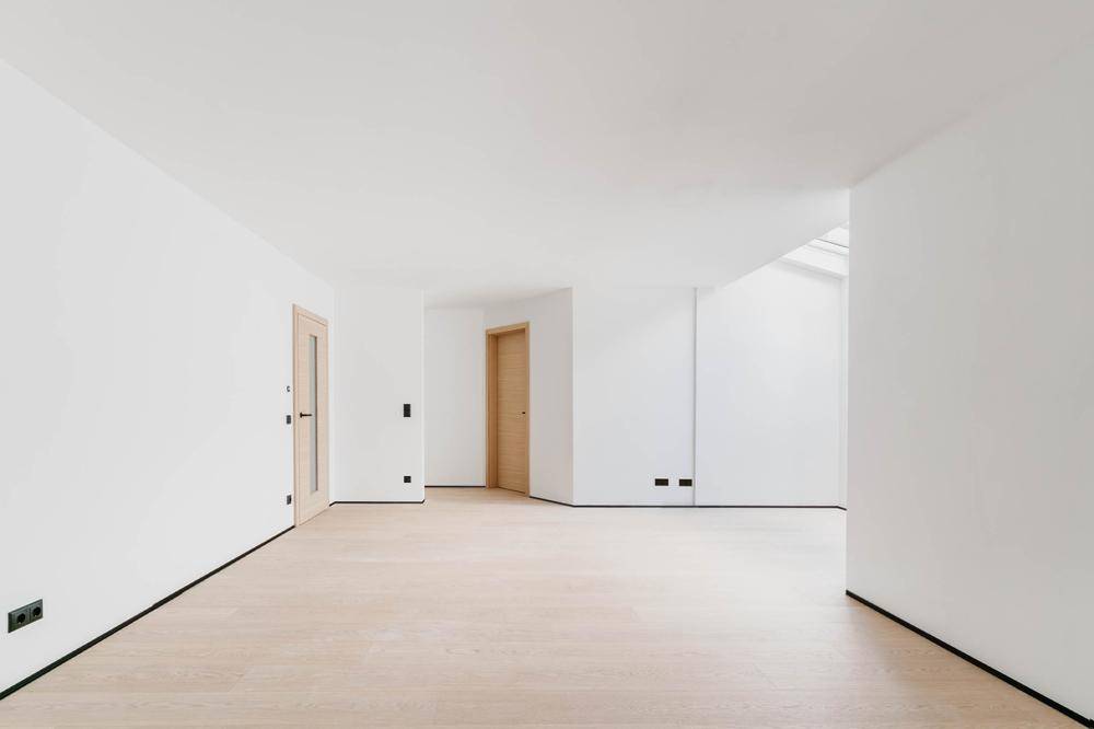 Heller, leerer Raum mit Holzboden, mehreren Türen und einem Dachfenster für natürliches Licht.