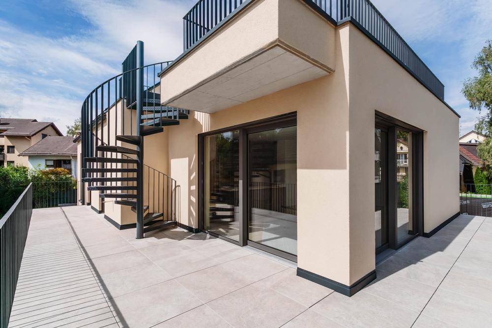Außenansicht eines modernen Gebäudes mit großer Terrasse und einer eleganten Wendeltreppe.