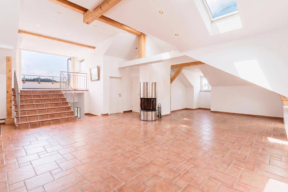 Geräumiger Wohn-Essbereich mit Terrakottafliesen, Kamin und sichtbaren Holzbalken unter Dachschrägen.