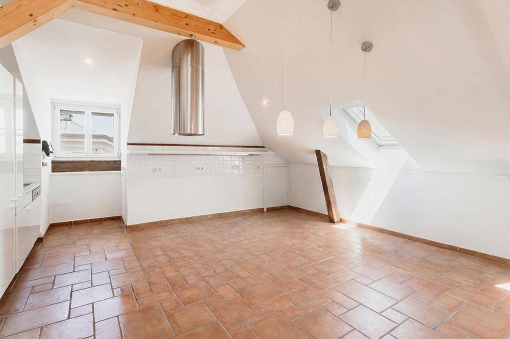 Unmöblierte Küche mit Terrakottafliesen, Dachschrägen und sichtbaren Holzbalken, bereit zur Einrichtung.