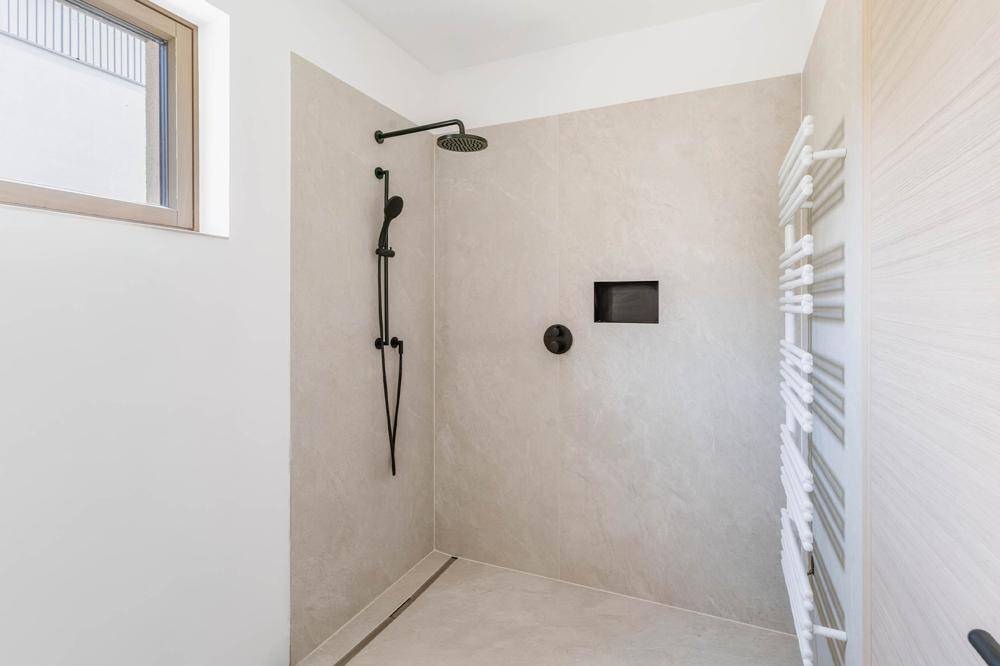 Modernes Badezimmer mit ebenerdiger Dusche, schwarzen Armaturen und beheiztem Handtuchhalter.