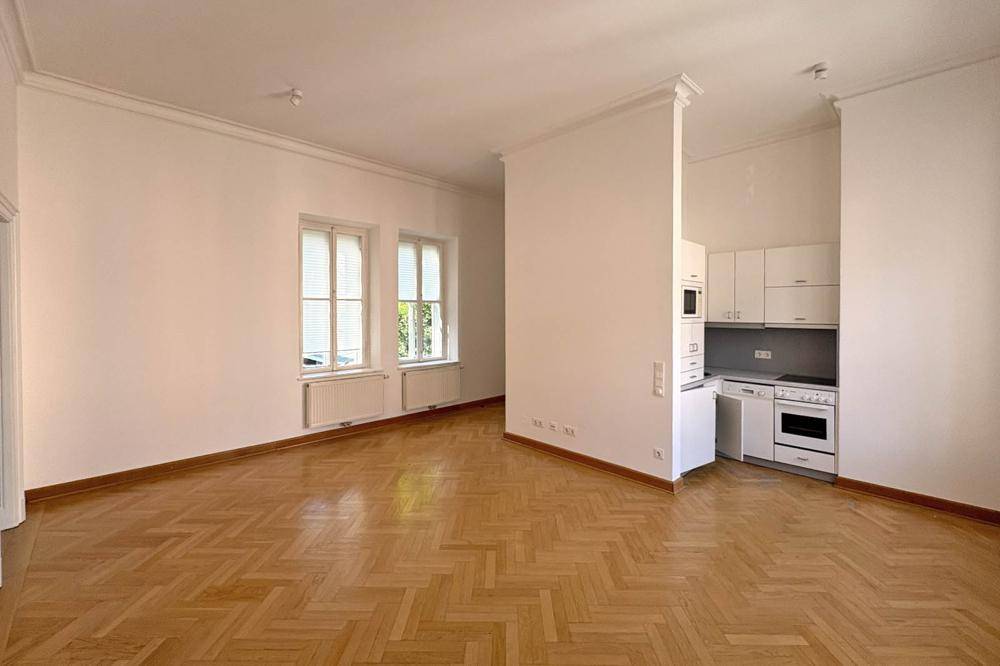 Heller Wohnbereich mit Fischgrätparkett und integrierter Küchenzeile, ideal für offenes Wohnen.