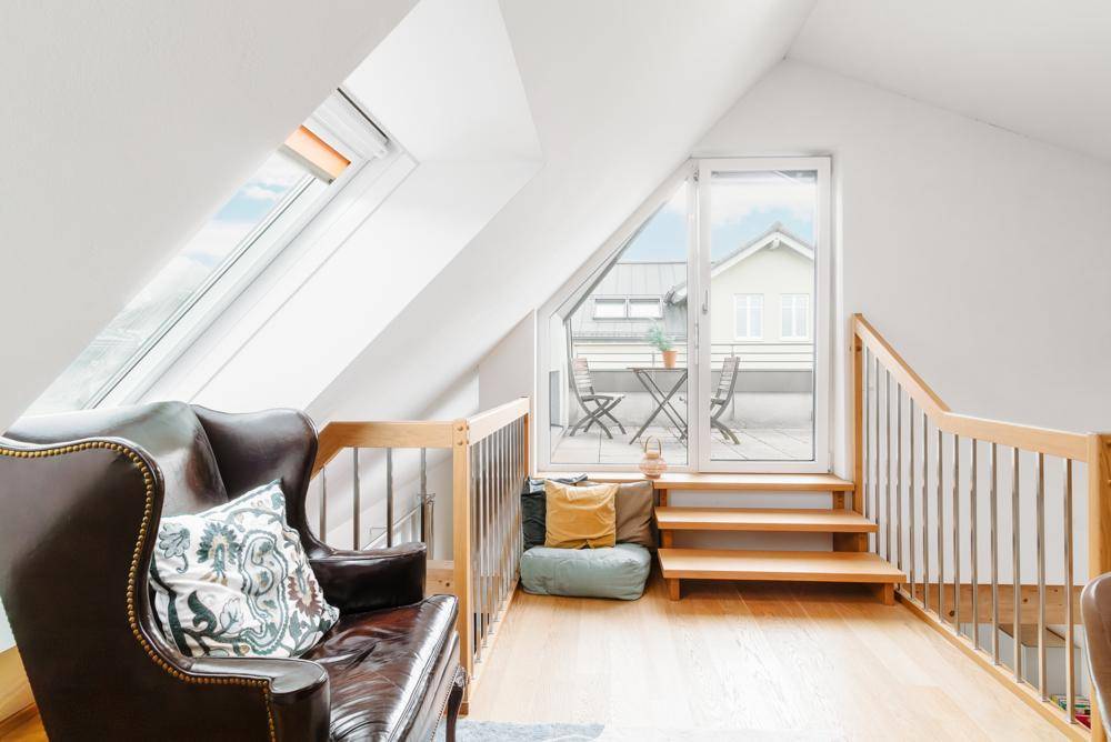 Heller Galeriebereich mit bequemen Ledersessel, Dachfenstern und Zugang zu einer Dachterrasse.