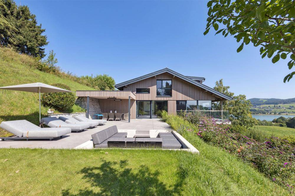 Geräumige Terrasse mit modernen Lounge-Möbeln und weitem Blick auf den See und die Landschaft.