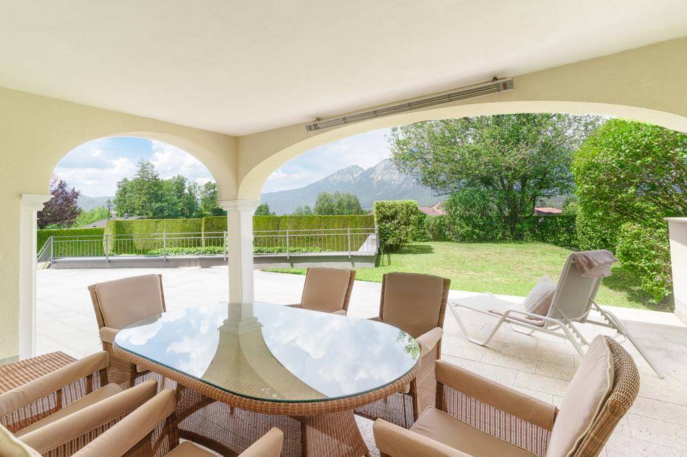 Überdachte Terrasse mit Rattanmöbeln und Blick auf die umliegende grüne Landschaft und Berge.