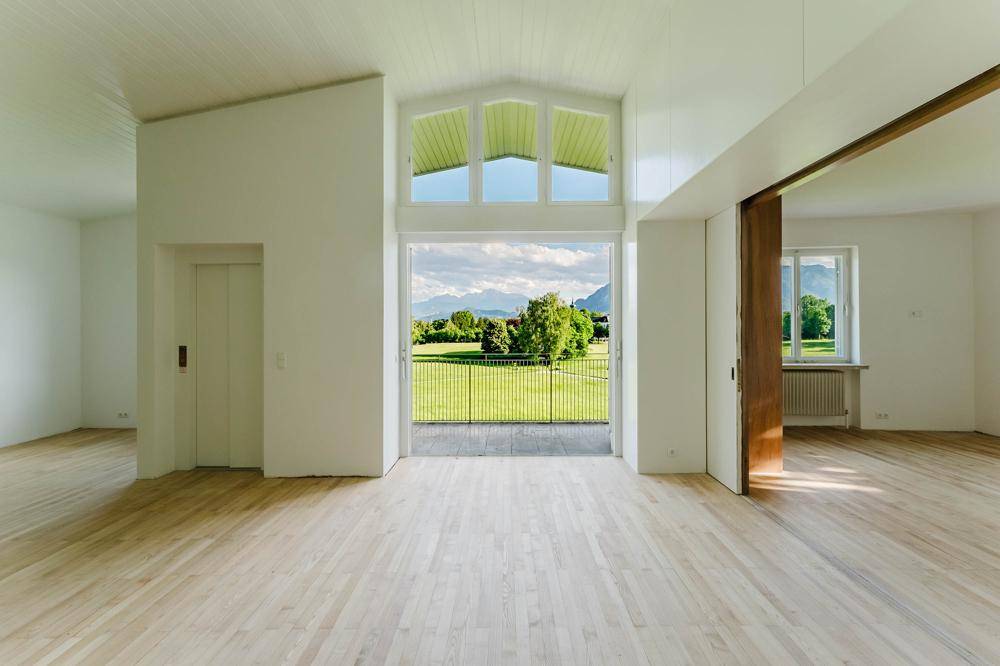 Lichtdurchfluteter Wohnbereich mit hohen Decken, Holzboden und Panoramafenstern zur Landschaft.