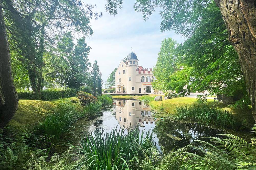 Malerisches Anwesen mit historischem Turm, umgeben von einem idyllischen Teich und altem Baumbestand.
