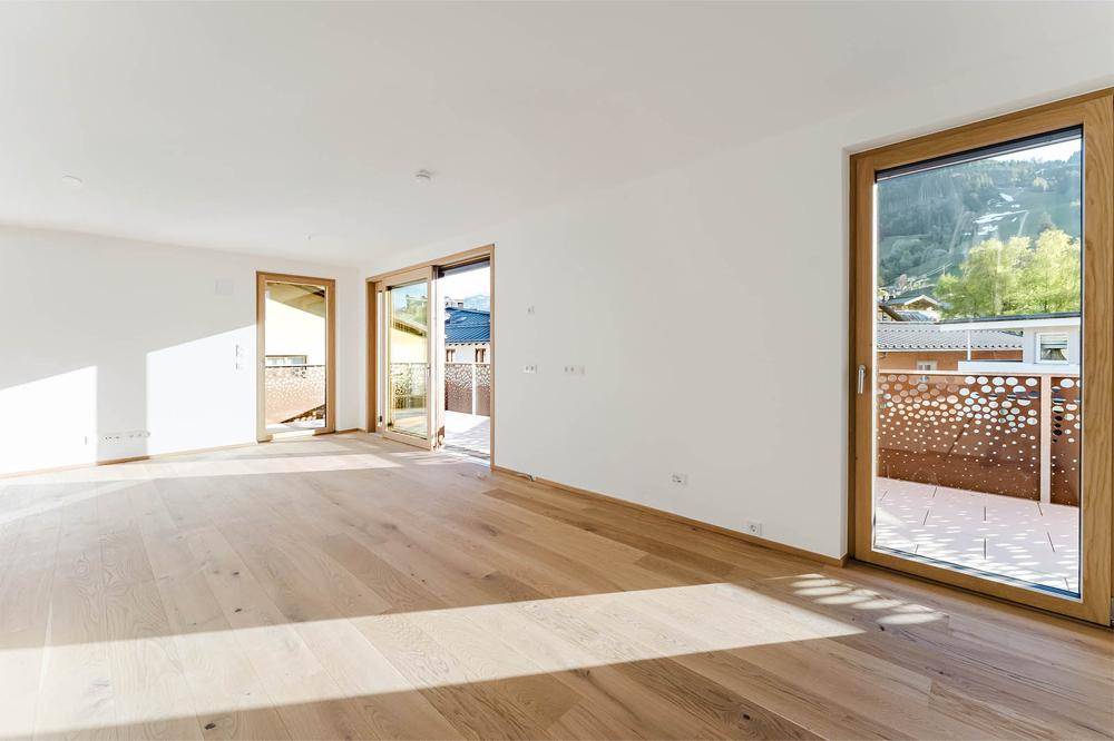 Lichtdurchfluteter Raum mit Holzboden und mehreren Zugängen zu Balkonen, bietet vielseitige Nutzungsmöglichkeiten.