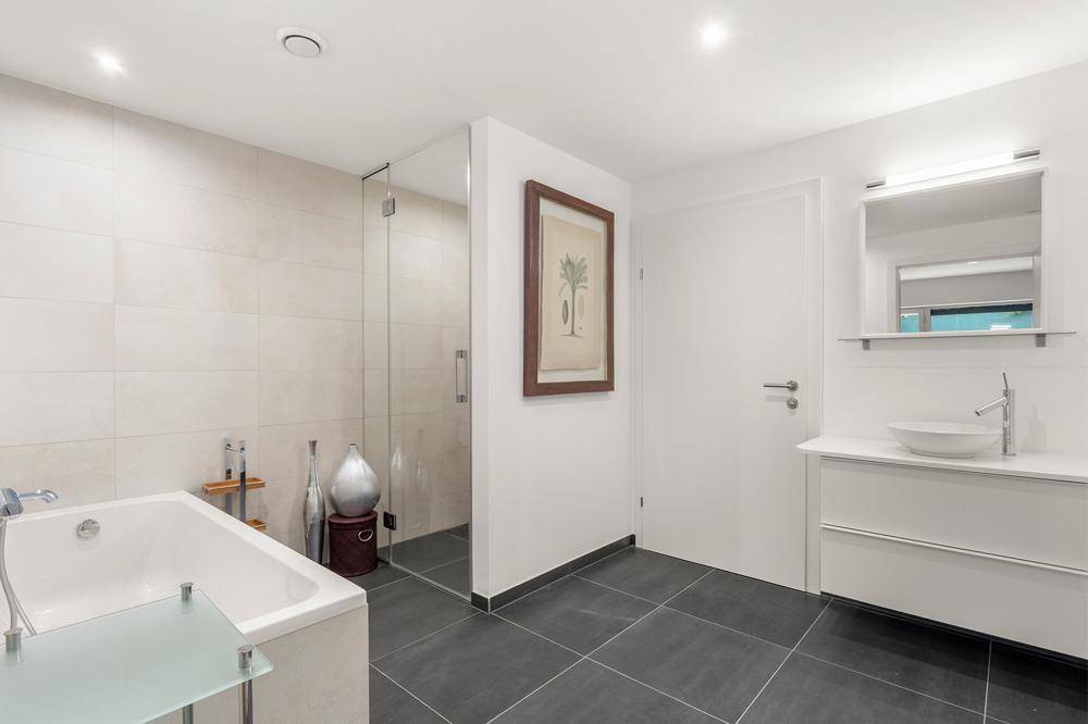 Modernes Badezimmer mit Badewanne, Duschbereich und hellem Fliesenboden.