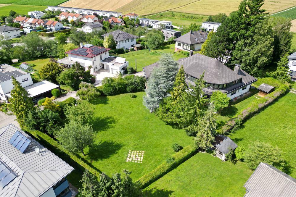 Weitläufiger Gartenbereich mit gepflegtem Rasen und altem Baumbestand, umgeben von einer Wohnsiedlung.