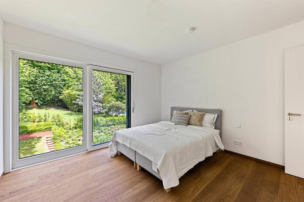 Gemütliches Schlafzimmer mit Holzboden und großem Fenster mit Blick auf den Garten.