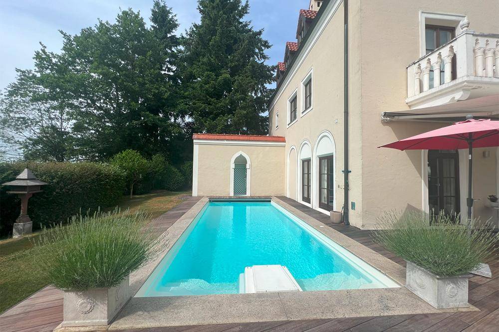 Langer, schmaler Pool auf einer Holzterrasse, umgeben von mediterranen Pflanzen und Grünflächen.