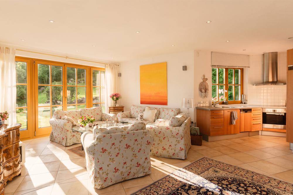 Sonniger Wohnbereich mit floralen Sofas, offener Holzküche und direktem Zugang zum Garten.