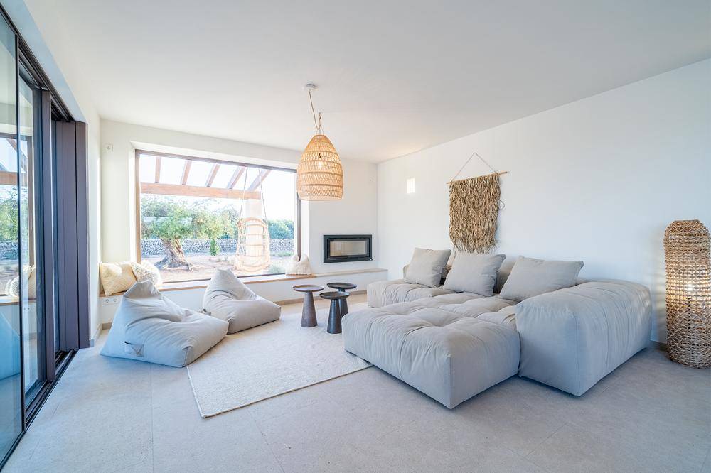 Gemütliches Wohnzimmer mit großem Sofa, Kamin und weitem Blick in den Garten durch Panoramafenster.