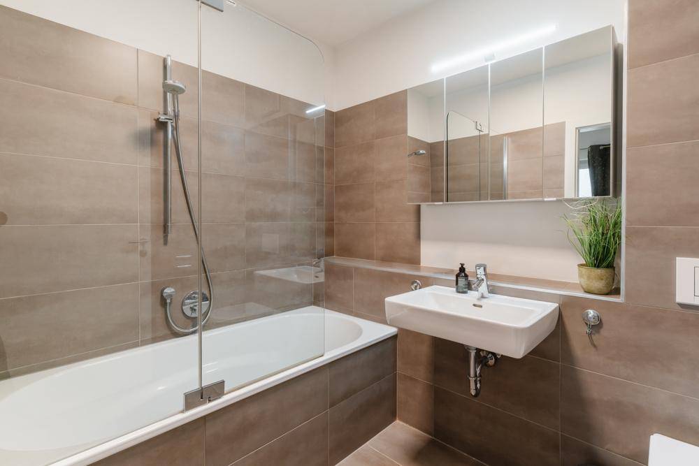 Modernes Badezimmer mit braunen Fliesen, Badewanne mit Duschfunktion und Spiegelschrank.