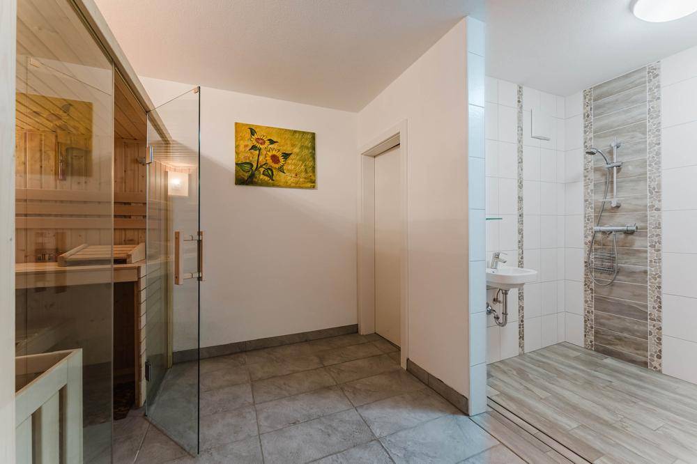 Wellnessbereich mit moderner Sauna, Dusche und kleinem Waschbecken.