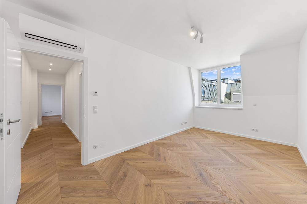 Schlafzimmer mit Fischgrätparkett, Dachschräge und Fenster, das viel Tageslicht hereinlässt.