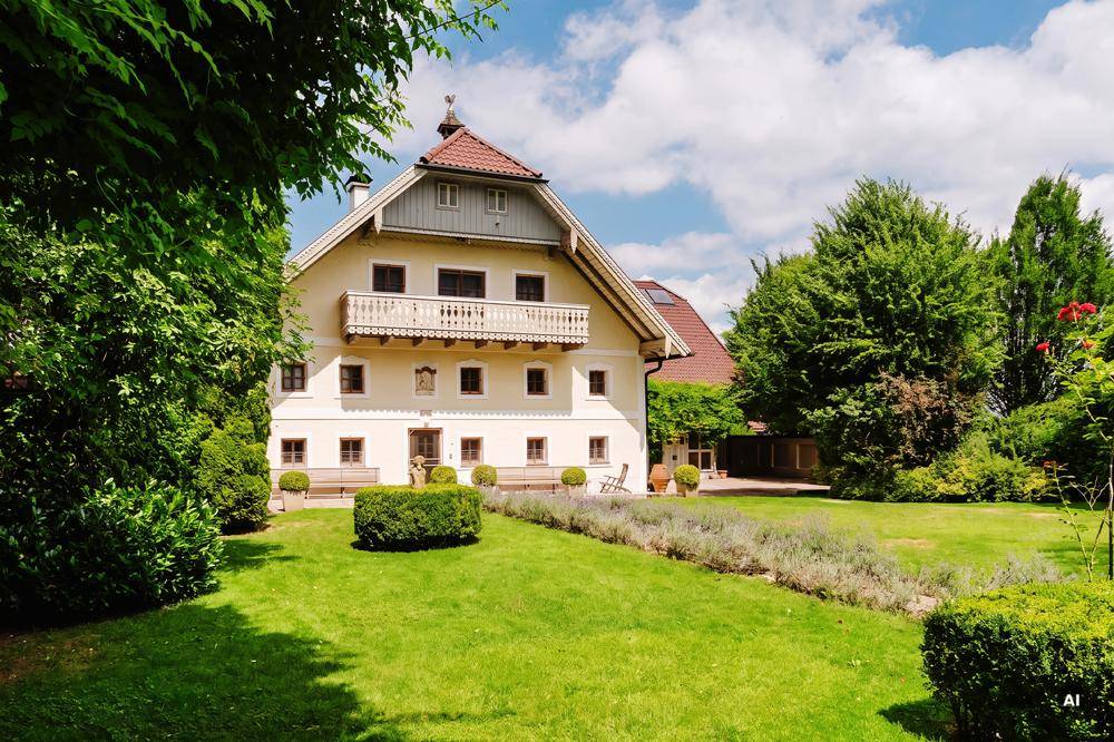 Weitläufiger, gepflegter Garten mit Rasenflächen und Hecken vor dem charmanten Landhaus mit Balkon.