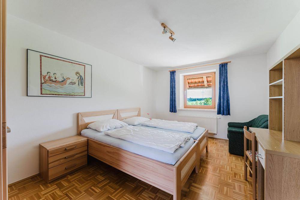 Helles Schlafzimmer mit Doppelbett aus Holz, Nachttisch und Schreibtisch, ausgestattet mit Parkettboden.