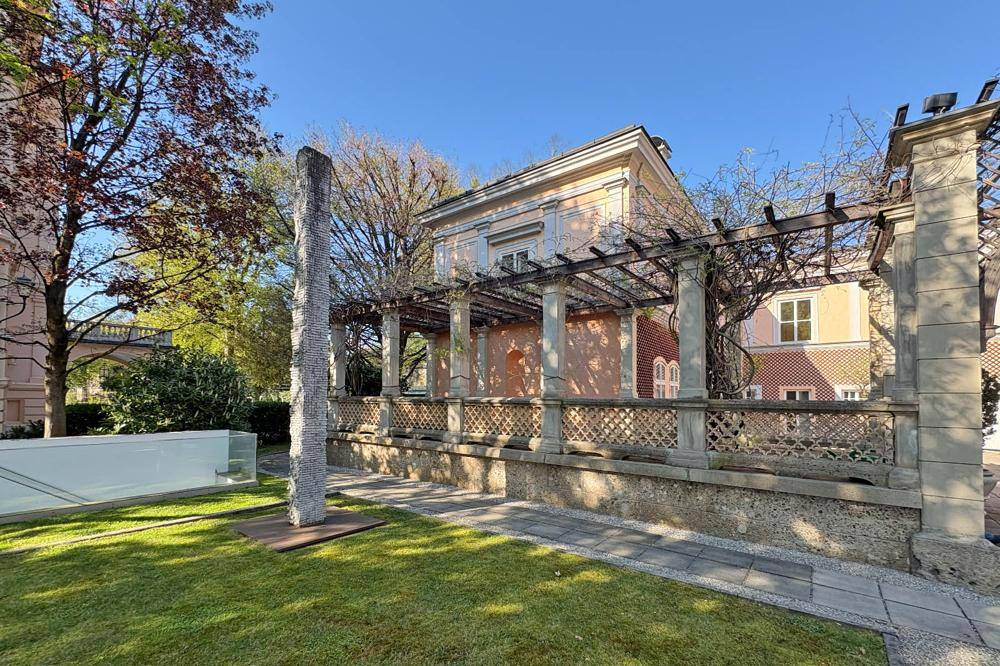 Gepflegter Gartenbereich mit Rasenfläche, Pergola und historischer Architektur im Hintergrund.