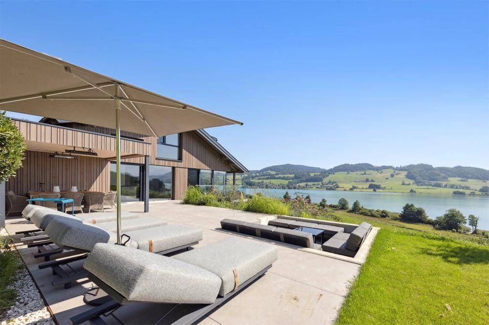 Sonnige Terrasse mit bequemen Liegen und einem beeindruckenden Panorama über den See.