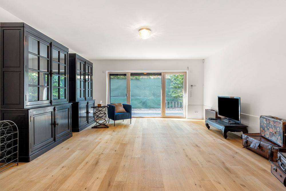 Geräumiges Wohnzimmer mit dunklen Schränken, Holzboden und Zugang zum Außenbereich.