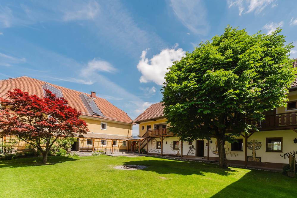 Sonniger Innenhof mit Rasenfläche, großem Baum und traditionellen Holzveranden, umgeben von den Gebäuden.