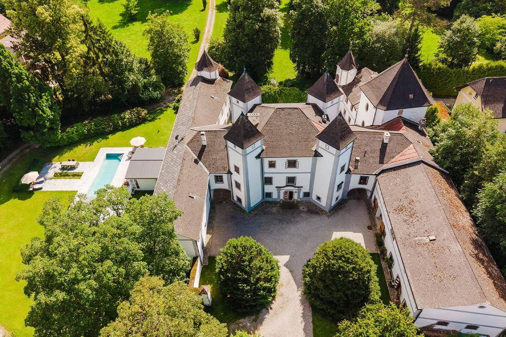 Luftaufnahme eines weitläufigen historischen Anwesens mit Innenhof, umgeben von viel Grün und einem Poolbereich.