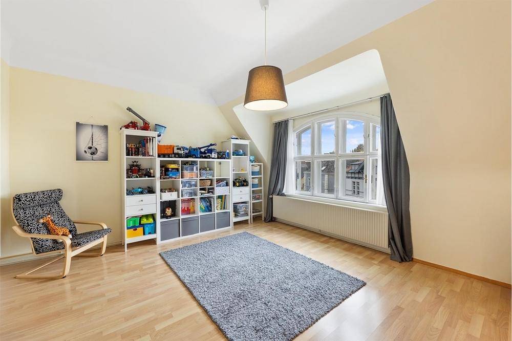 Helles Kinderzimmer im Dachgeschoss mit Laminatboden, Schrägen und Spielzeugregalen.