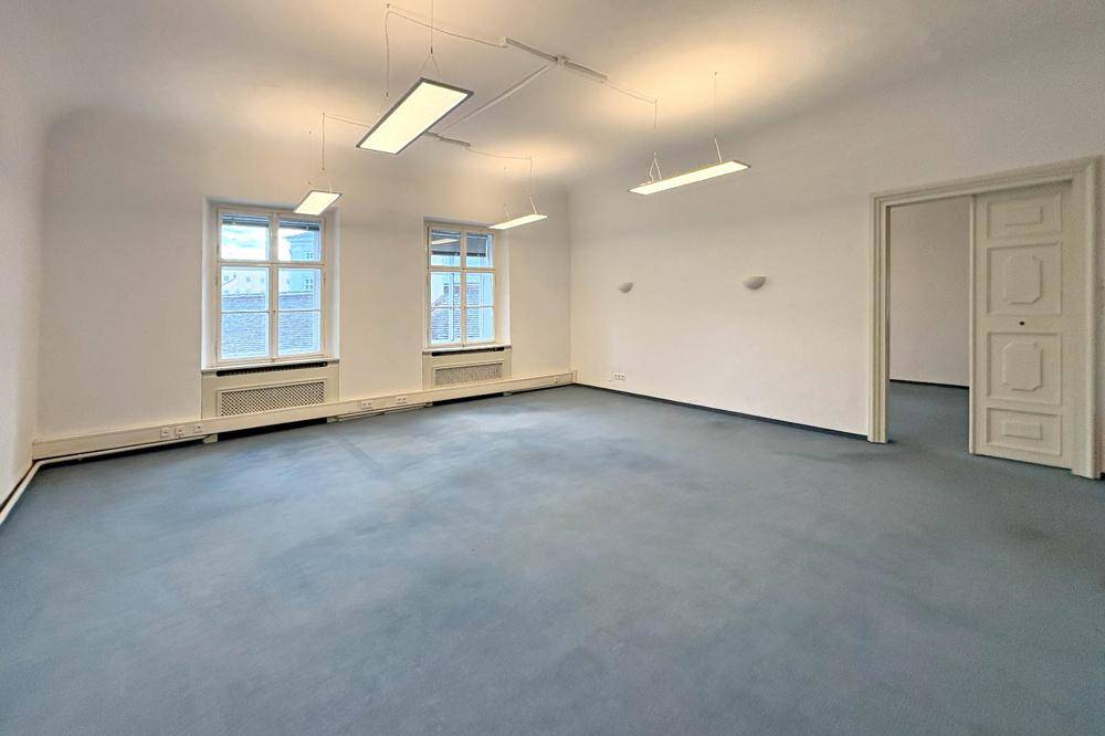 Geräumiges Zimmer mit blauem Teppichboden, hohen Decken und zwei Fenstern.