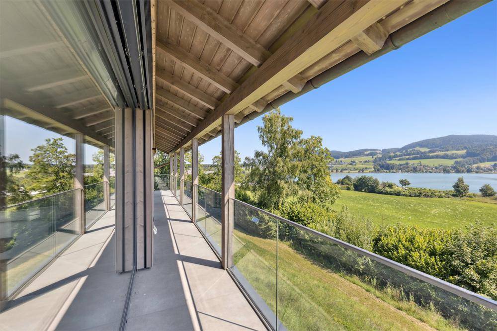 Überdachte Loggia mit Glasgeländer und Panoramablick auf den See und die umliegende Natur.