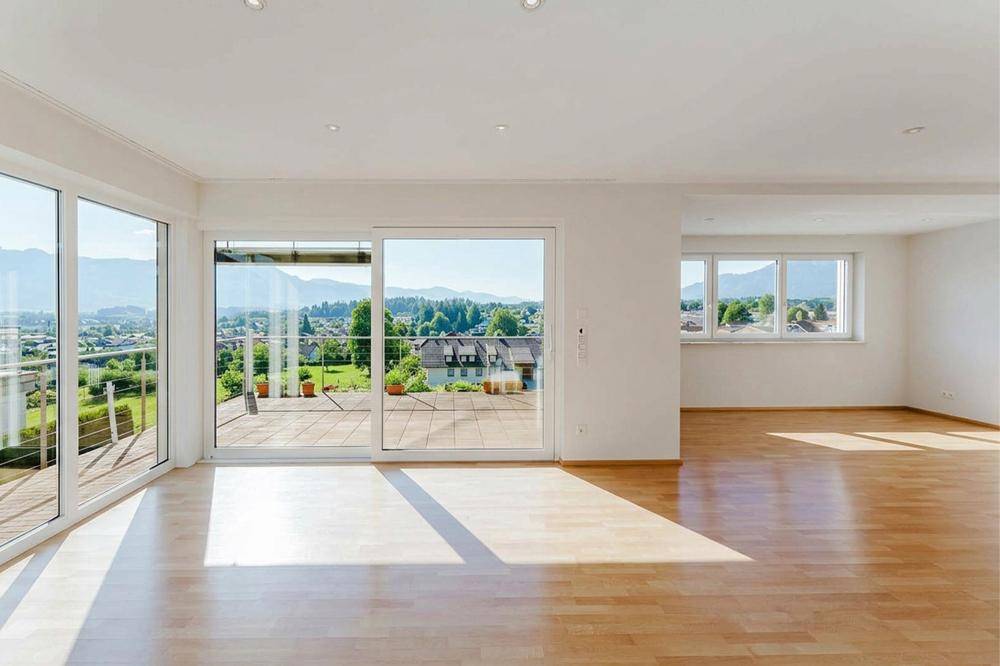 Helles Wohnzimmer mit Holzboden, großen Fensterfronten und Panoramablick auf die Berge.