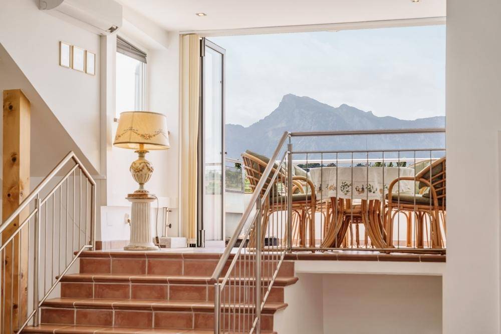 Heller Treppenaufgang mit Terrakottafliesen und Zugang zu einem Balkon mit beeindruckendem Bergblick.