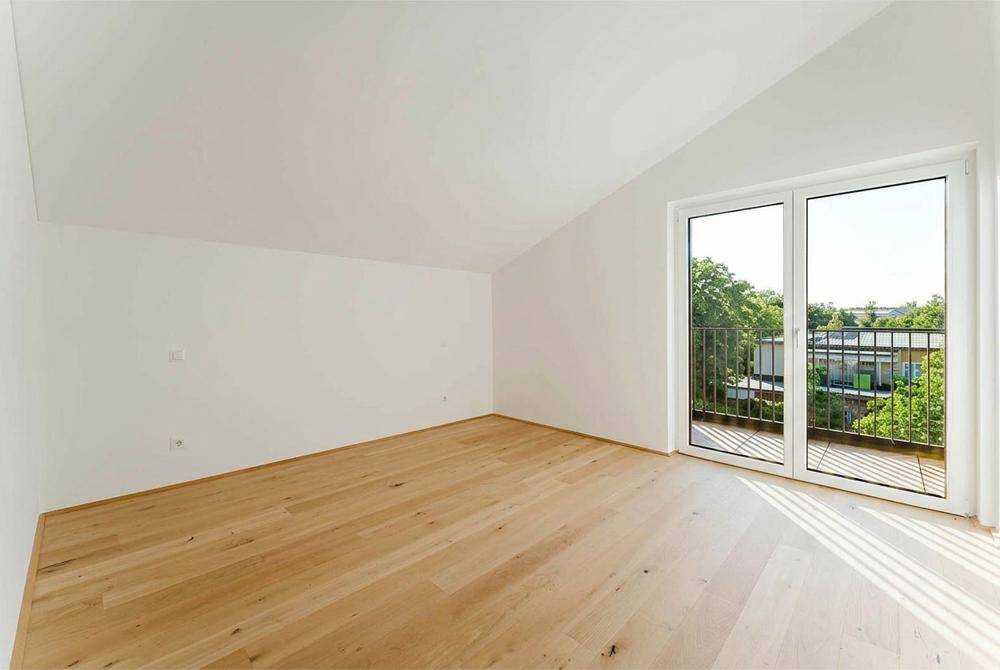 Helles Zimmer mit Holzboden, Dachschräge und direktem Zugang zu einem Balkon.