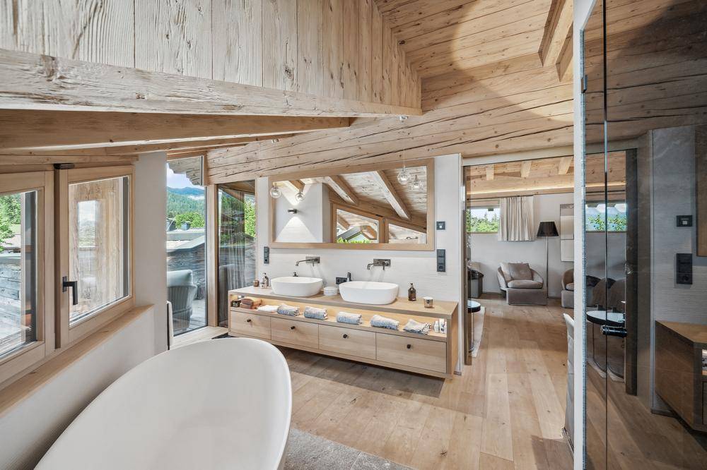 Luxuriöses Badezimmer mit Doppelwaschbecken, freistehender Badewanne und großen Fenstern mit Bergblick.