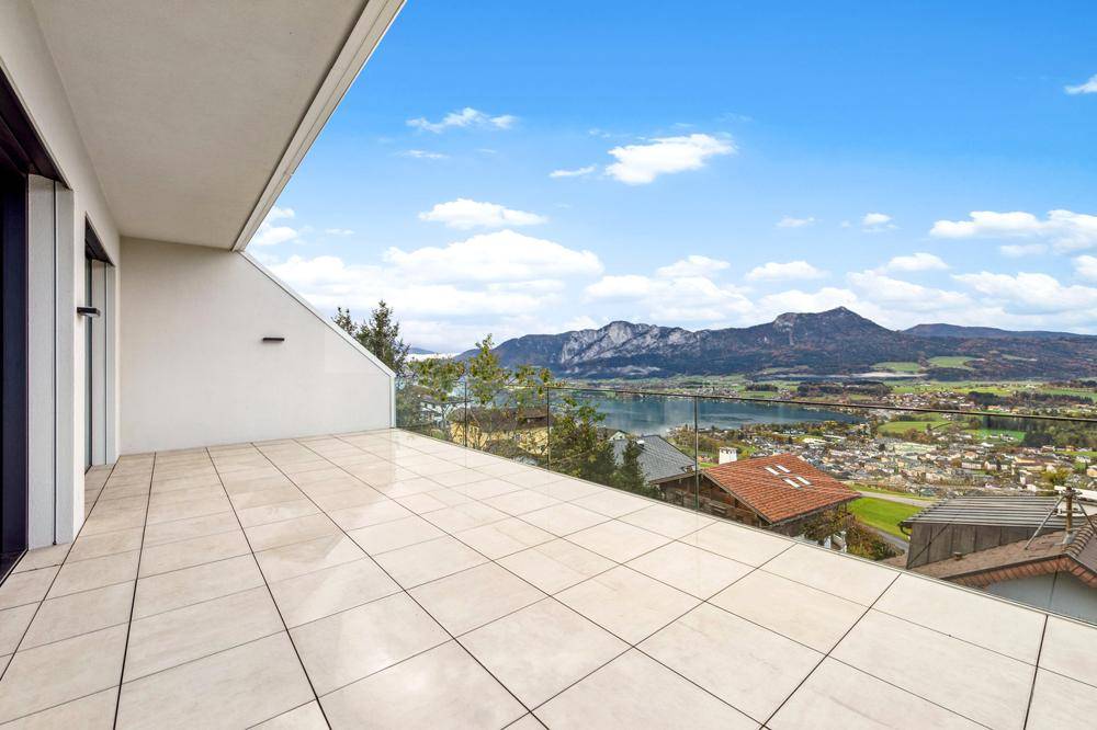 Geräumige Terrasse mit Glasgeländer und atemberaubendem Blick auf See und Berge.