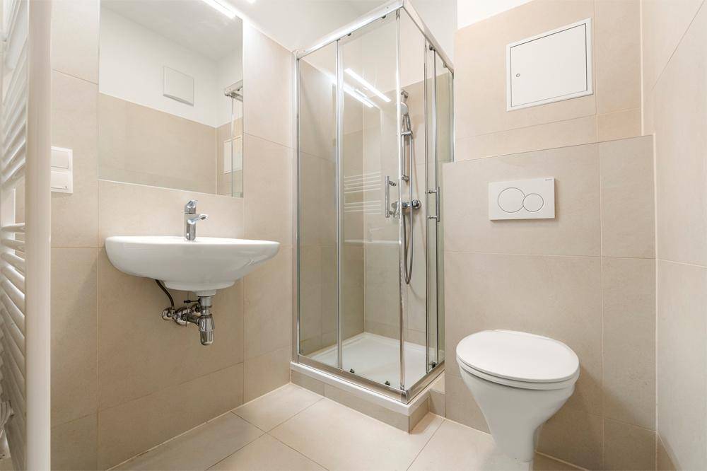 Modernes Badezimmer mit beigefarbenen Fliesen, Duschkabine, wandhängendem WC und Handtuchheizkörper.